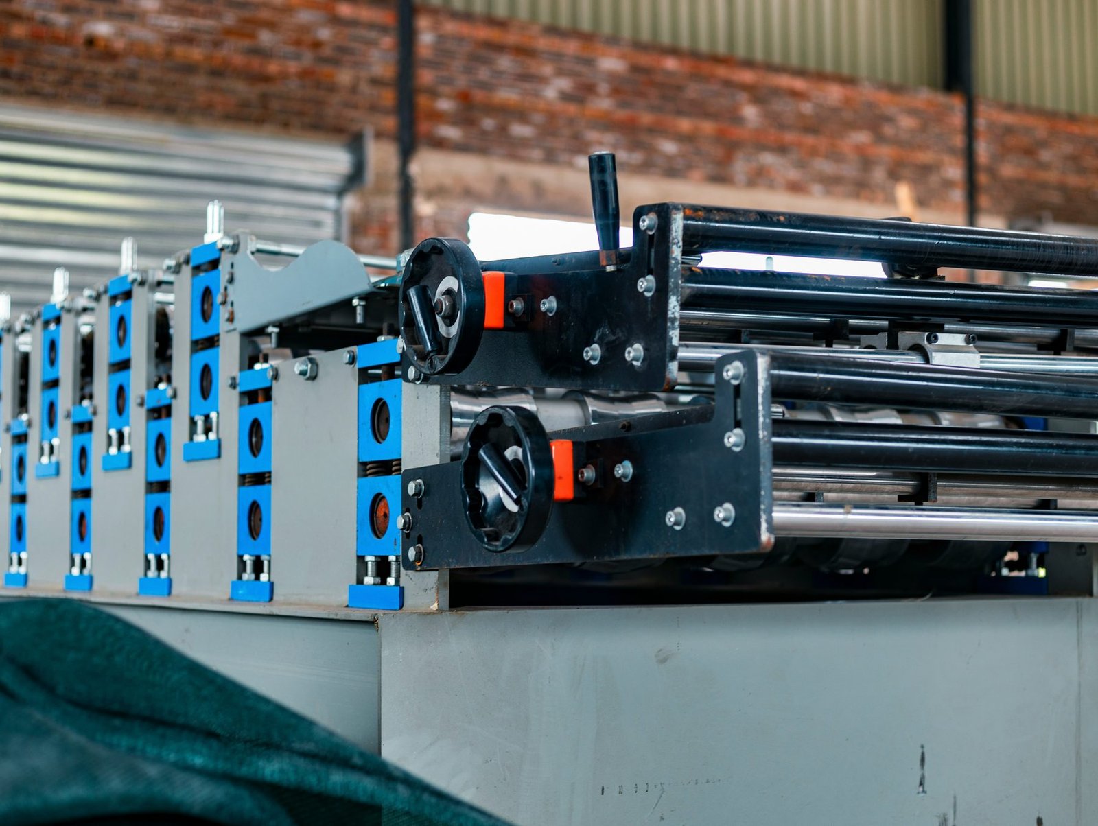 A metal roll-forming machine with blue fittings in a brick workshop