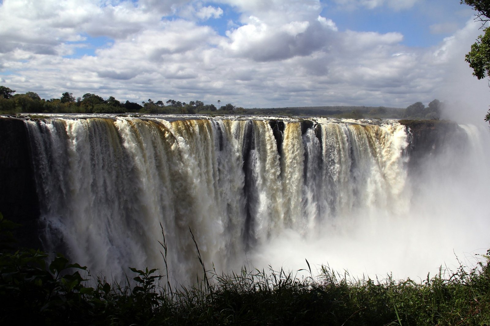 Victoria Falls in flood, the full width of the curtain pouring into the gorge beneath broken cloud
